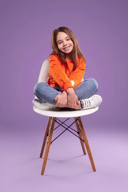 Photo of Cute small girl sitting on chair and smiling at camera