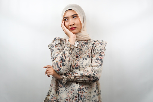 Beautiful asian young muslim woman thinking, looking for ideas, looking for solutions to problems, with hands holding cheeks, isolated on white background
