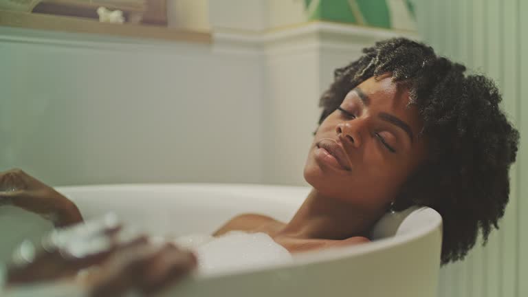 Beautiful African ethnicity woman relaxing in modern bathroom. Wearing moisturizing gel eye patches and meditating