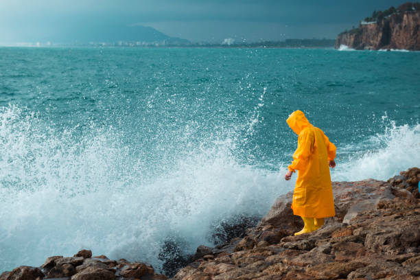 Man in yellow raincoat walking on breakwaters in stormy weather. Stormy weather in the port. rain, storm, bad weather landscape