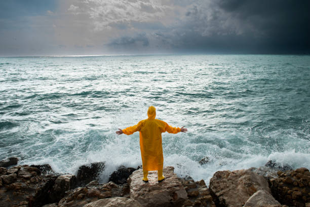 istock Storm clouds, high waves and man in yellow raincoat. 1356614318