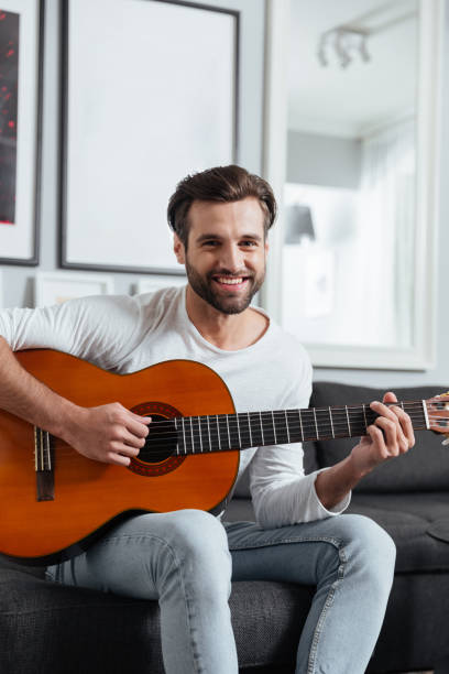 istock Happy man sitting on sofa playing on guitar. 1356617508