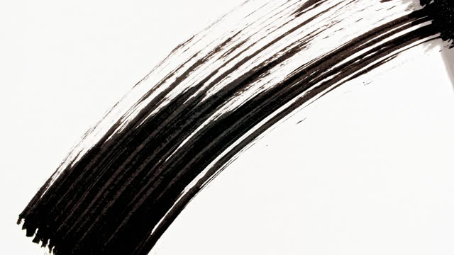 Macro shot and slow motion of a black mascara isolated on white background. Advertising professional cosmetics. Closeup of a mascara wand on white background