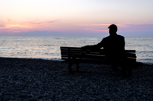 silhouette of a man sitting on a bench by the sea during the evening sunset. beautiful sky on a spring day