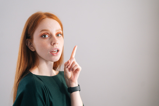 Retrato de una bonita modelo joven pelirroja señalando con el dedo a la cámara sobre fondo blanco. photo