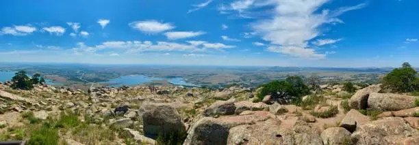 Panoramic view of plains from mountain overlook with boulders in foreground under blue sky and clouds (shot taken from Mount Scott, Wichita Mountains Wildlife Refuge, Oklahoma)