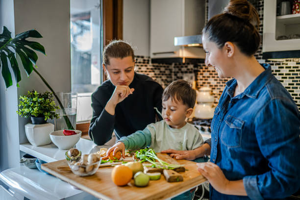 same sex couple and their child preparing dinner in kitchen - homosexual family lesbian parent imagens e fotografias de stock