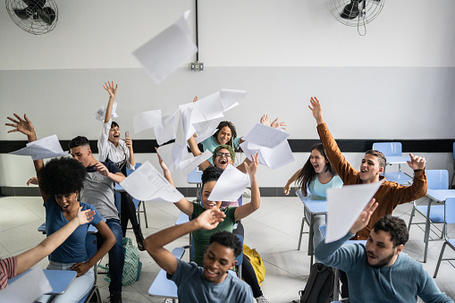 Teenager students throwing paper in the air in the classroom