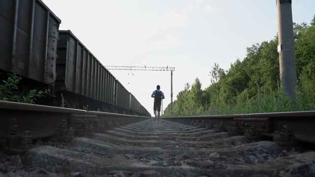 man traveler with backpack walks far along rails of railway near passing train