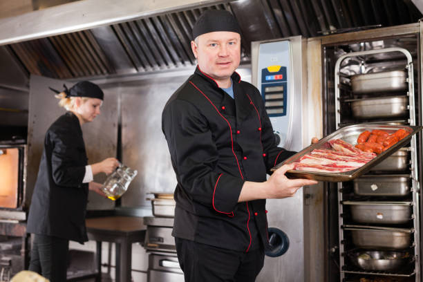 istock Cook putting pork ribs and sausages into oven 1356634317