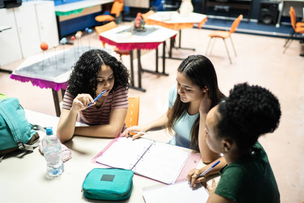 teenage students doing homework together in the classroom - pen color image black book imagens e fotografias de stock