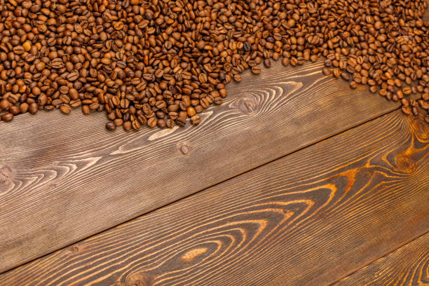 roasted coffee beans laid on brown wooden table surface with copy space in diagonal linear perspective with seelctive focus