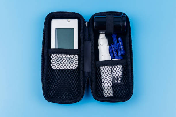 istock Home blood glucose test kit in carrying case on pastel blue background. Digital glucometer, lancet pen, disposable needles and test strips in black case. Top view. Diabetes concept 1356645197