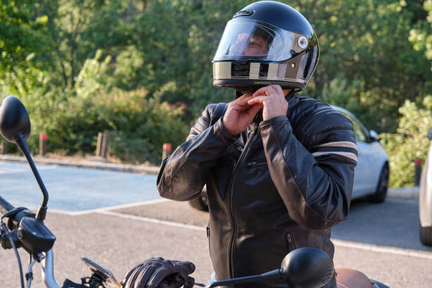 ein biker setzt einen helm auf, bevor er auf dem motorrad fährt - sturzhelm stock-fotos und bilder