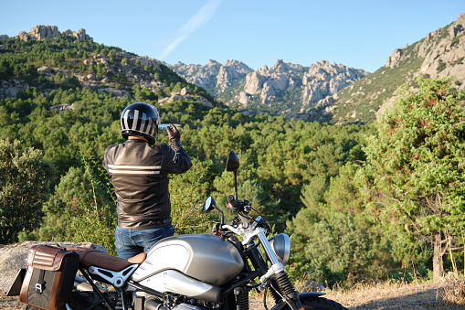 Man riding a motorcycle taking a photo with a smartphone in nature.