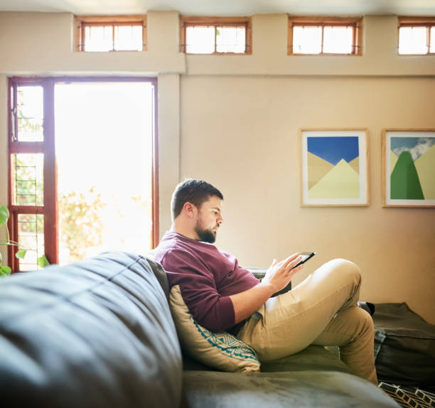 istock Young man relaxing on living room sofa using digital tablet 1356655705
