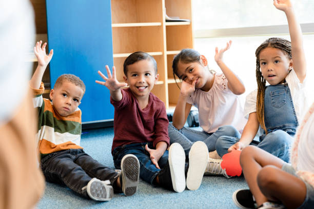 istock Multi-ethnic group of kindergarten age children raise hands 1356661400