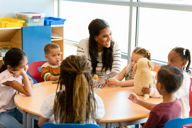 Smiling teacher teaches children about the solar system A cheerful mid adult preschool or kindergarten teacher smiles as she teaches a group of children about the solar system. A little girl is playing with a solar system model. teacher stock pictures, royalty-free photos & images