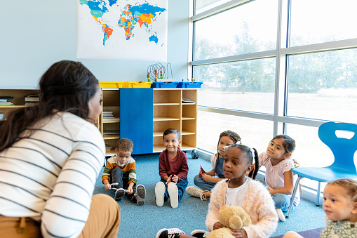 A cheerful kindergarten teacher tells a story to a group of attentive school children.