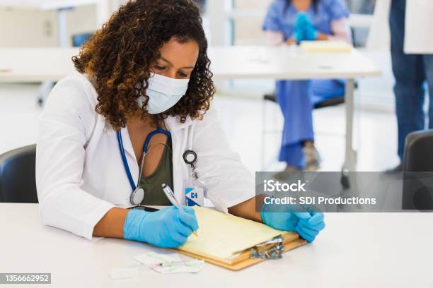 Volunteer Doctor Writes In Patient Chart Stock Photo - Download Image Now - Healthcare And Medicine, Latin American and Hispanic Ethnicity, Lifestyles