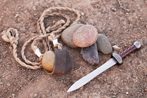 La honda de David con cinco piedras lisas y la espada de Goliat en la tierra photo