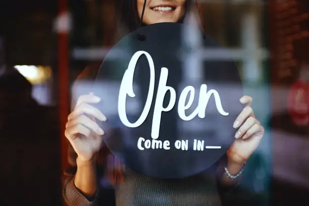 Photo of Young manager girl changing a sign from closed to open sign on door cafe