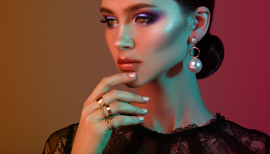 High Fashion model woman in colorful bright lights posing in studio. Portrait of beautiful sexy girl wearing jewelry with trendy make-up On colourful vivid background