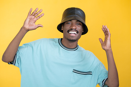 Happy hipster man. Hip-hop style. Friendly meeting. Positive guy in rapper look leather hat sportive sweatshirt isolated yellow.