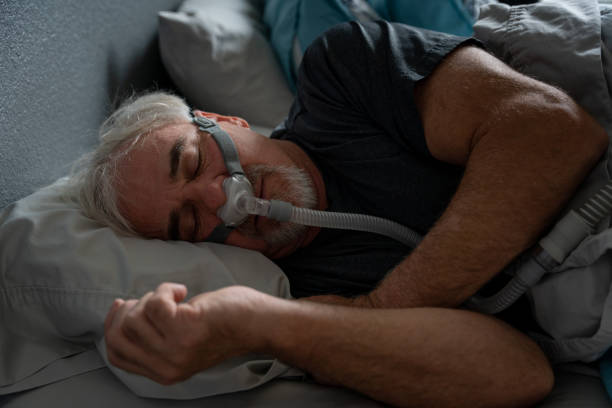 hombre maduro con apnea del sueño que usa una máscara cpap en la cama durmiendo - apnea del sueño fotografías e imágenes de stock