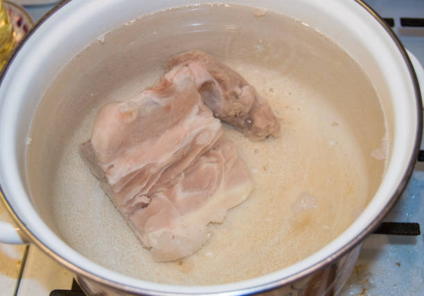 A piece of raw meat in a white enameled saucepan close-up, cooking homemade meat broth stock photo