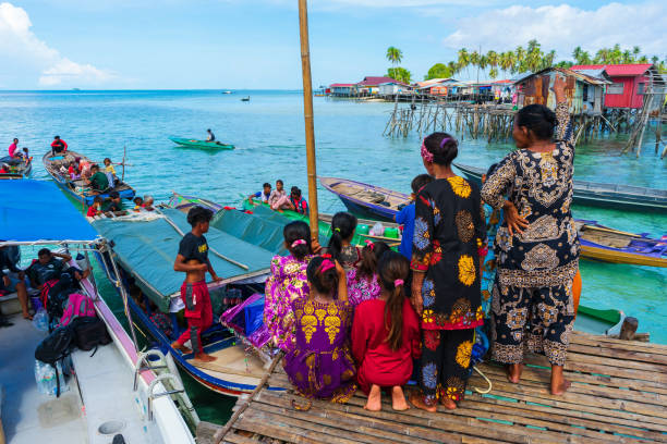 Bajau Laut women in colorful clothes on the bamboo jetty where boats drop off passengers. stock photo
