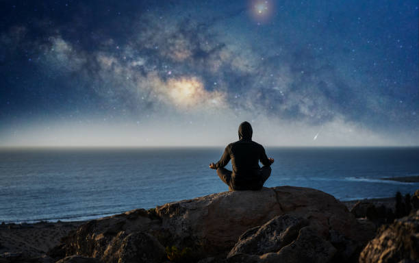 person meditating at night under the milky way moon and shooting star - climbing men sea cliff imagens e fotografias de stock