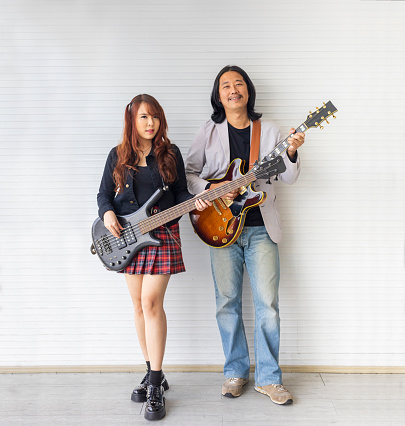Portrait of Asian family duo rock band of young girl idol on bassist and male on semi hollow electric guitar standing on white background for music, artist, musician
