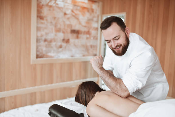lächelnde therapeutin, die einer sportlerin eine sport-ellenbogenmassage gibt - massage table massaging sport spa treatment stock-fotos und bilder