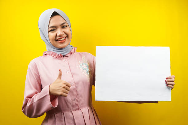 Pretty young muslim woman cheerful holding blank empty banner, placard, white board, blank sign board, white advertisement board, presenting something in copy space, promotion stock photo