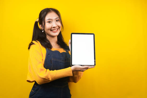 Pretty and cute young woman cheerful, confident, with hands holding tablet, with blank or white screen tablet, presenting something, promoting product, advertisement, isolated stock photo