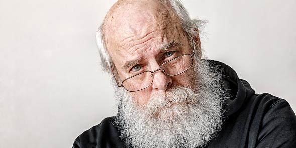 Long gray beard senior adult man portrait. He's wearing a black hoody-type sweatshirt.
