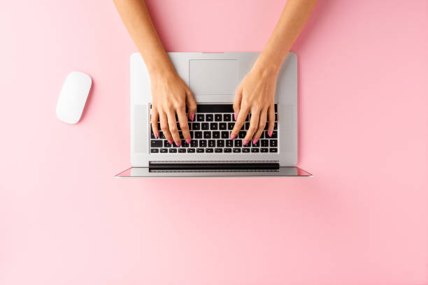 istock Overhead shot of woman’s hands using laptop on pink table. Office desktop. Flat lay 1356716212