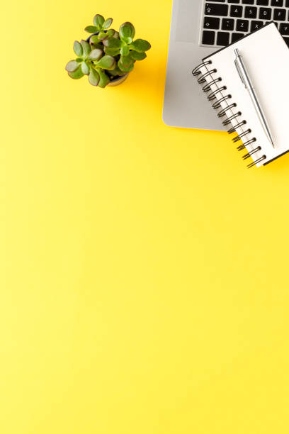 istock Modern office desktop with laptop, notebook and pen on yellow background. Business background 1356716406