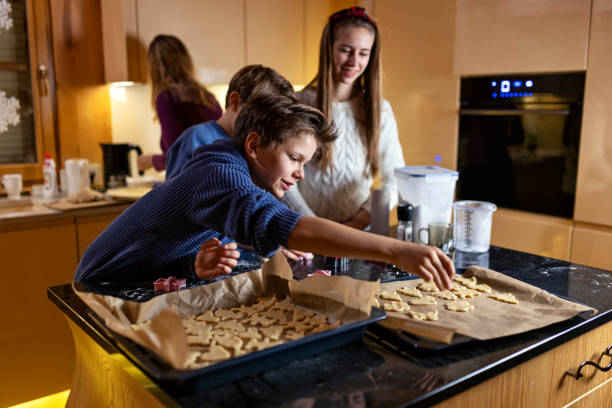 мама и трое детей делают печенье на кухне - baking paper cookie tray стоковые фото и изображения