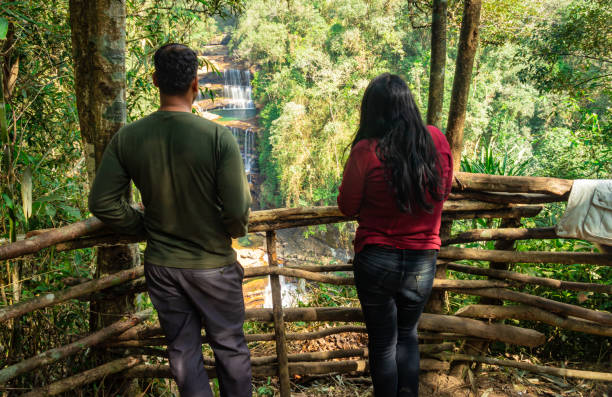 istock young couple watching waterfall falling from mountain top in green forests at morning from top angle 1356725333
