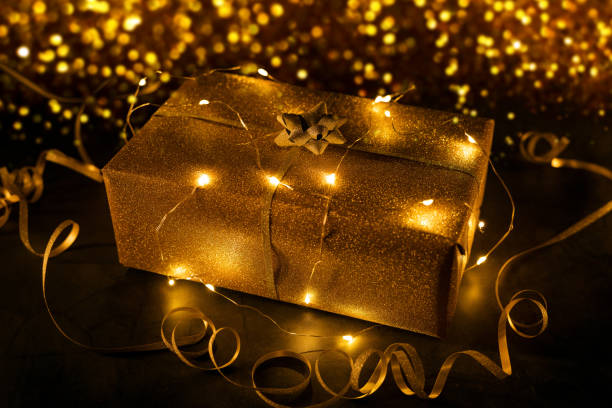 cadeau en or emballé dans des guirlandes lumineuses sur fond bokeh doré - wrapped package string box photos et images de collection