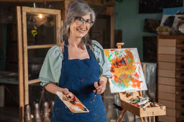 istock Artist smiling flirtatiously and holding palette with paints while standing 1356736971
