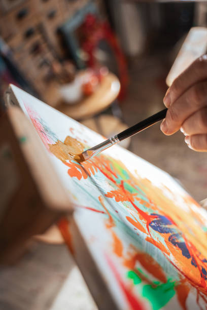istock Unrecognizable woman holding brush and mixing paints on the canvas while drawing 1356736987