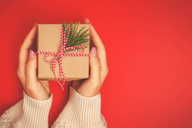istock Christmas gift in women's hands on a red background 1356737107