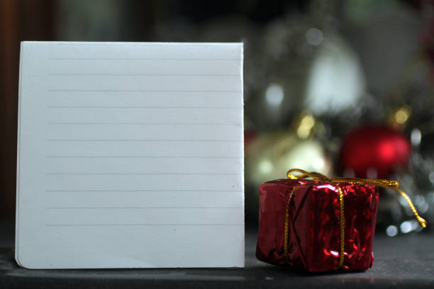 Red christmas gift box with ribbon and a blank notepaper on the table, for your text message, personal letter, self note or inspirational quote.