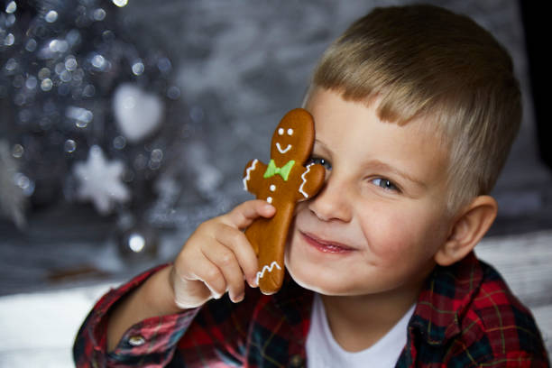 Adorable cheerful toddler hides behind Christmas gingerbread among festive decorations. Atmospheric, aesthetic home for New Year's Eve. Good mood. Cheerful baby boy. Joyful, warm cozy home concept