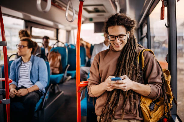 istock Young smiling hipster man using phone in public bus 1356742052