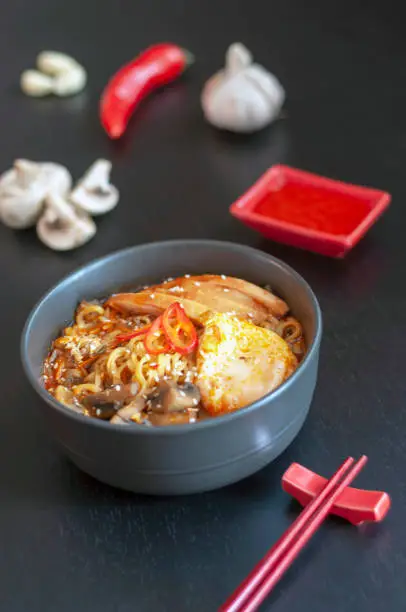 Photo of Ramen is a national, popular dish of traditional Korean cuisine with chopsticks and ingredients. Asian soup with noodles, chicken breast, egg, mushrooms, broth, hot sauce and spices. vertical shot.