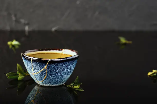Photo of Hot green tea bowl, Japanese tea on a dark background. Selective focus on the cup. Reclaimed ceramic blue cup, second life of things, recycling